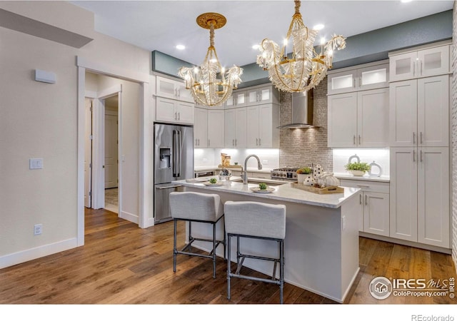 kitchen with appliances with stainless steel finishes, sink, hanging light fixtures, a center island with sink, and wall chimney exhaust hood