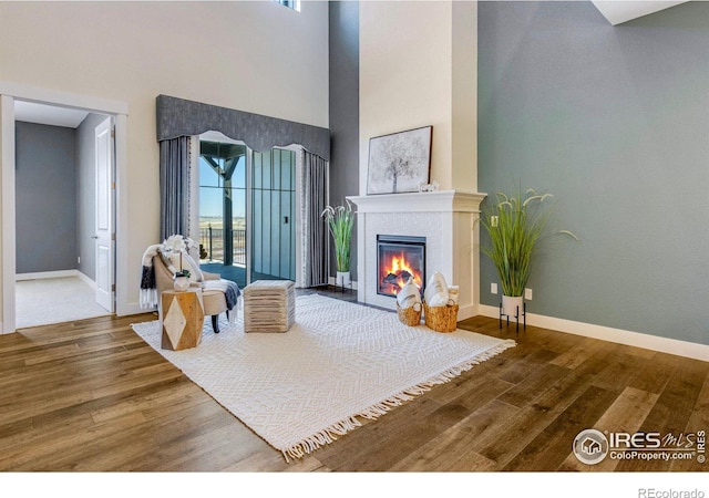 living room with a tiled fireplace, hardwood / wood-style flooring, and a high ceiling