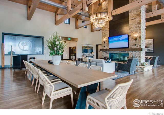 dining space featuring hardwood / wood-style flooring, an inviting chandelier, a high ceiling, a fireplace, and beamed ceiling