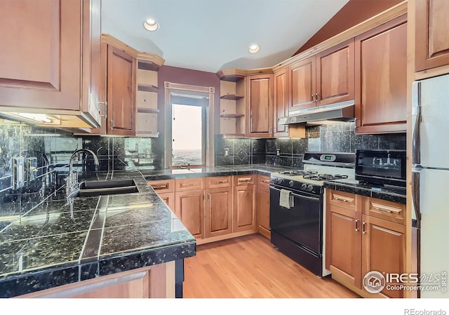 kitchen with sink, backsplash, white refrigerator, gas stove, and light wood-type flooring