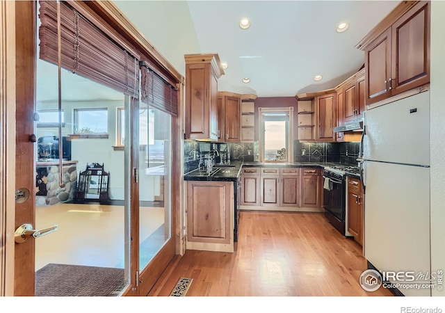 kitchen featuring black gas range oven, decorative backsplash, light hardwood / wood-style flooring, and white fridge