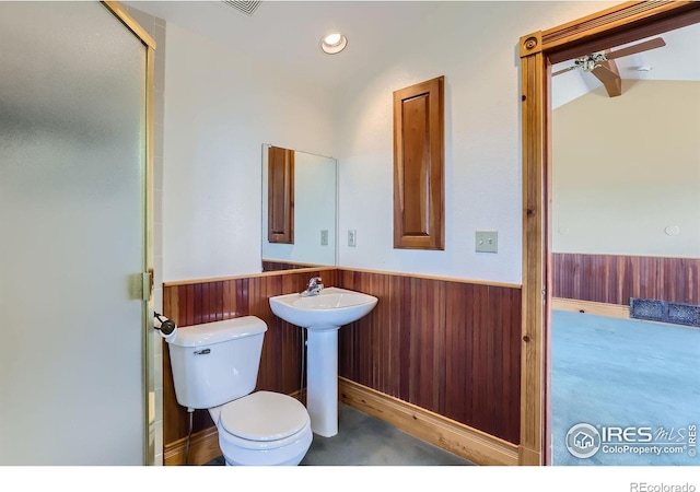 bathroom with toilet, a shower with shower door, ceiling fan, and wood walls