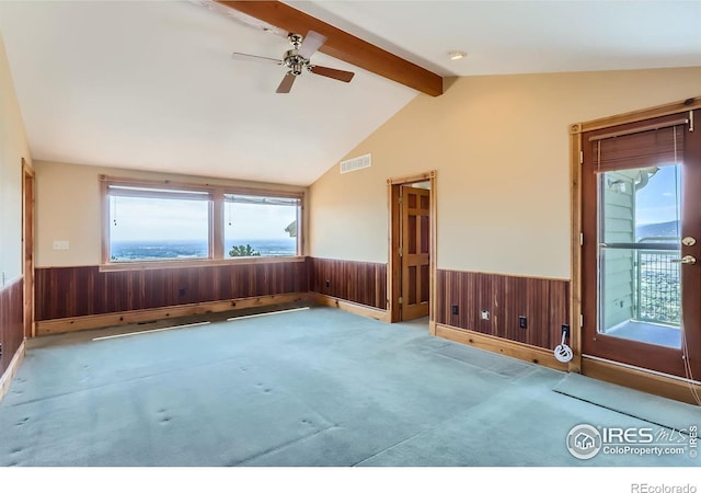 carpeted empty room featuring vaulted ceiling with beams, ceiling fan, and wood walls