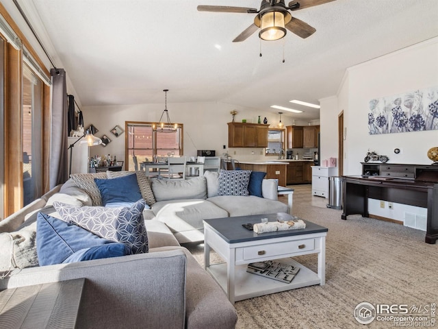 carpeted living room featuring ceiling fan with notable chandelier, sink, and vaulted ceiling