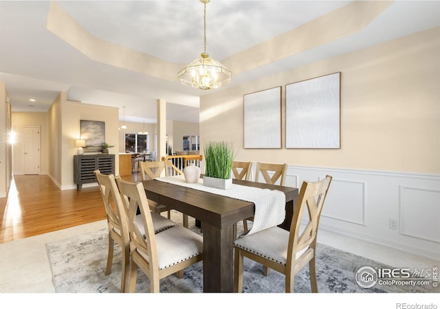 dining area featuring a raised ceiling, a notable chandelier, and light wood-type flooring