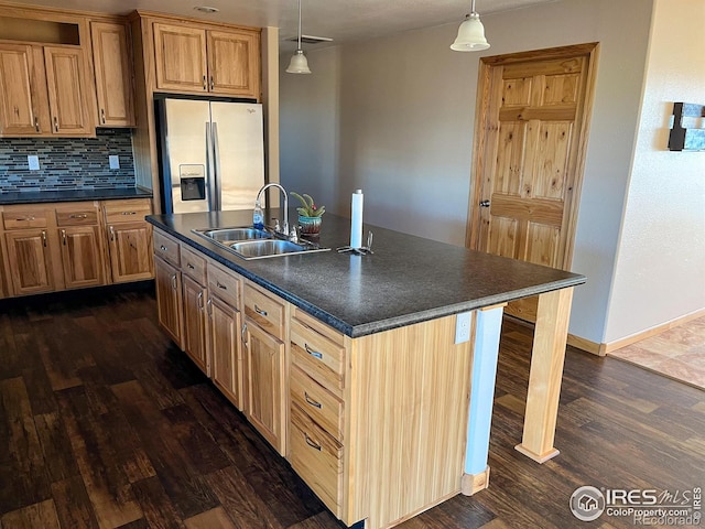 kitchen featuring pendant lighting, sink, stainless steel fridge, backsplash, and a center island with sink