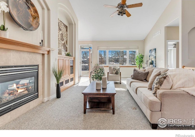 carpeted living room with a tiled fireplace, high vaulted ceiling, and ceiling fan