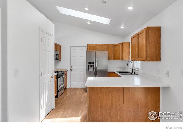 kitchen featuring sink, light hardwood / wood-style flooring, kitchen peninsula, stainless steel appliances, and vaulted ceiling with skylight