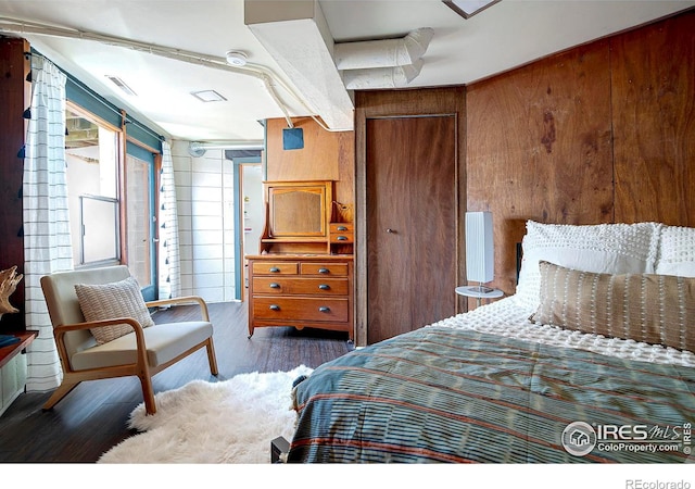 bedroom with dark wood-type flooring, wooden walls, and a closet