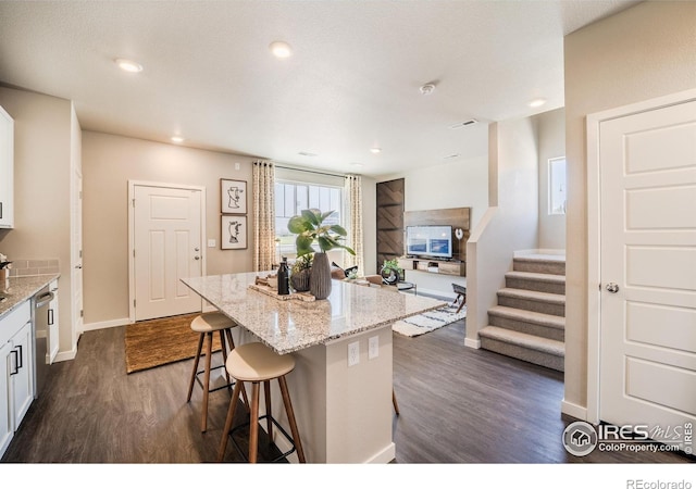 kitchen featuring a breakfast bar, white cabinetry, dark hardwood / wood-style flooring, a center island, and light stone countertops