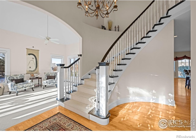 staircase featuring hardwood / wood-style floors, ceiling fan with notable chandelier, and a high ceiling