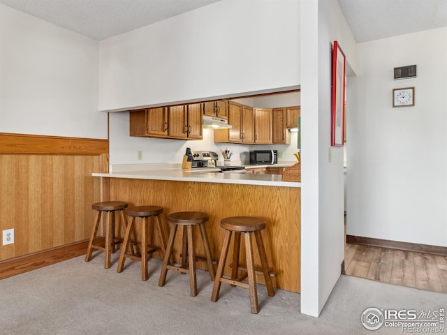 kitchen featuring a kitchen bar, stainless steel electric stove, kitchen peninsula, and light carpet