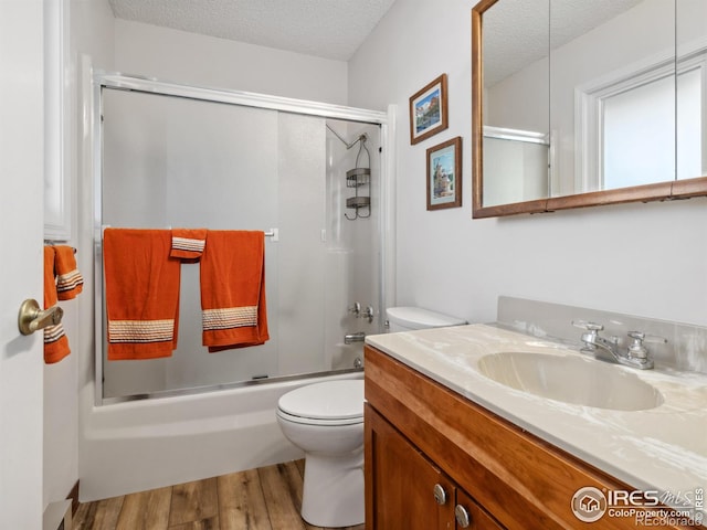 full bathroom with wood-type flooring, enclosed tub / shower combo, vanity, toilet, and a textured ceiling