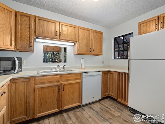 kitchen featuring sink, a textured ceiling, white appliances, and light hardwood / wood-style flooring