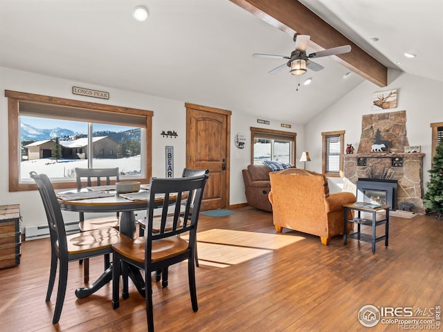 dining space with hardwood / wood-style flooring, ceiling fan, a stone fireplace, and vaulted ceiling with beams