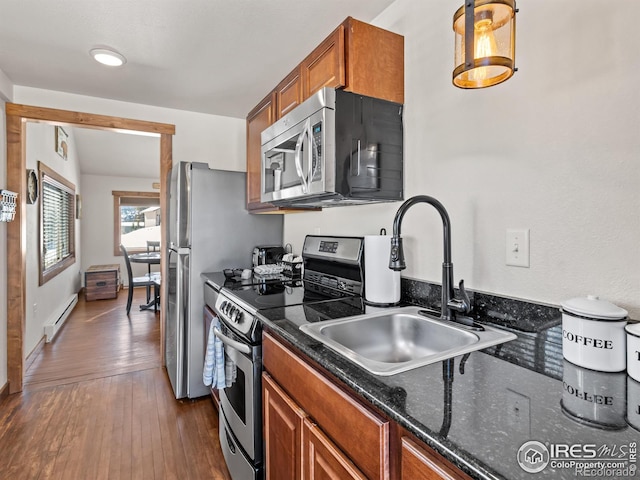 kitchen with sink, decorative light fixtures, baseboard heating, appliances with stainless steel finishes, and hardwood / wood-style floors