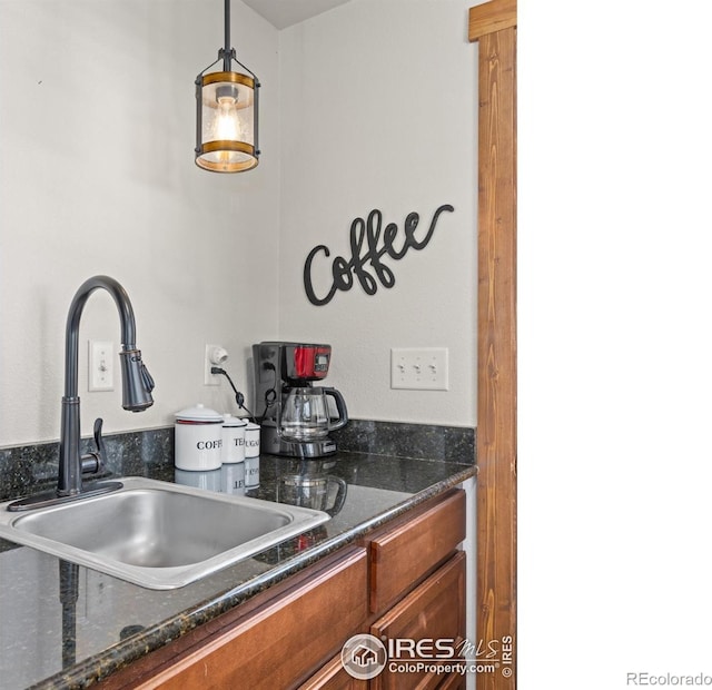 kitchen featuring dark stone counters, sink, and hanging light fixtures