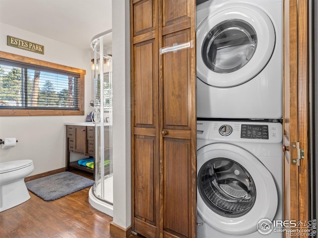 clothes washing area with stacked washing maching and dryer and dark wood-type flooring