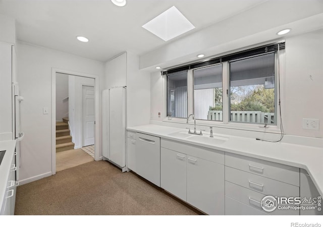 kitchen with a skylight, white cabinetry, dishwasher, sink, and light colored carpet