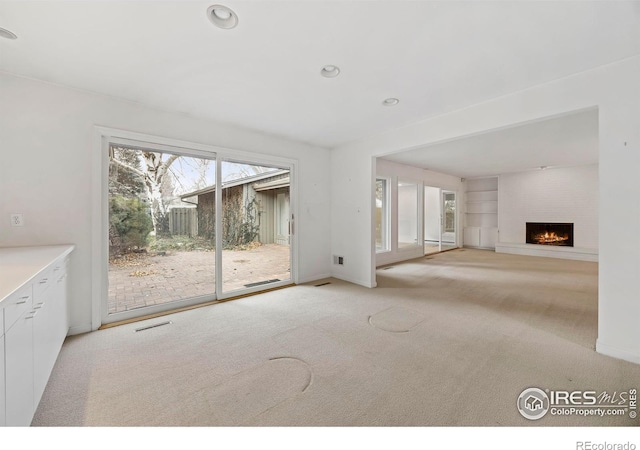 unfurnished living room with light carpet, built in features, and a fireplace