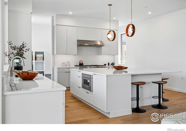 2125 Vine Ave, Boulder, CO 80304 - kitchen with under cabinet range hood, modern cabinets, light wood-style flooring, a kitchen island, and decorative backsplash