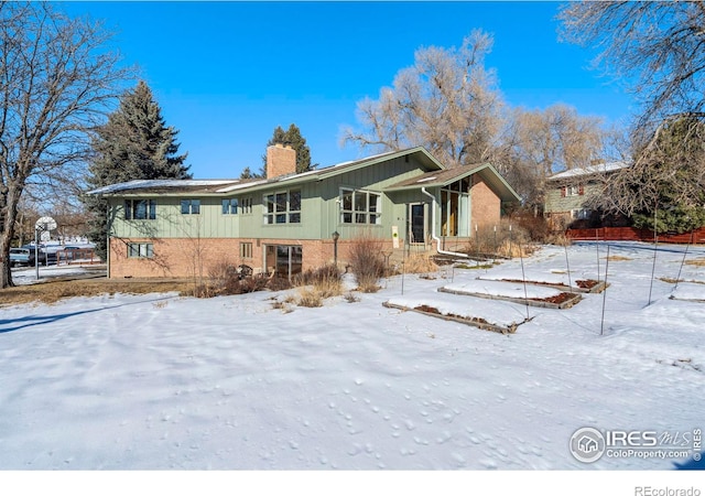 snow covered back of property featuring brick siding and a chimney