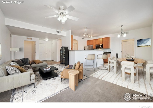 living room featuring ceiling fan with notable chandelier, light colored carpet, and rail lighting