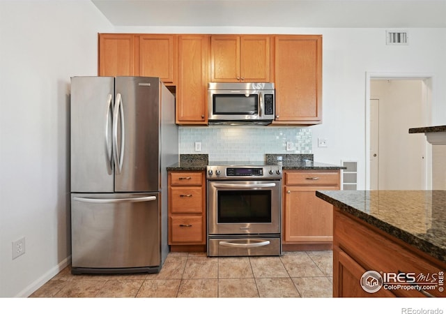 kitchen with appliances with stainless steel finishes, dark stone countertops, backsplash, and light tile patterned floors