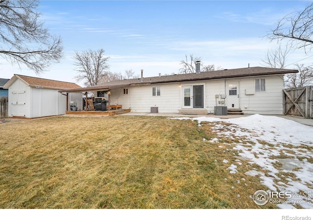 snow covered back of property with cooling unit, a yard, a deck, and a storage unit