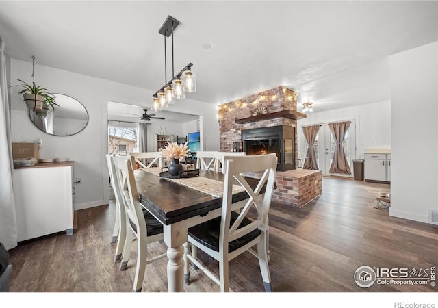 dining area featuring a brick fireplace, dark wood-type flooring, and ceiling fan