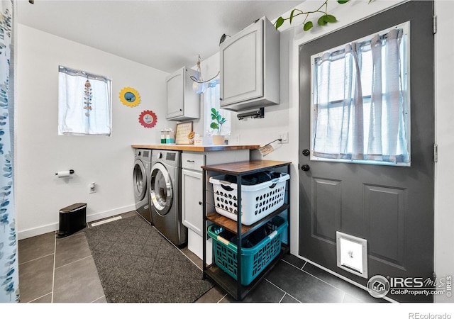 clothes washing area with cabinets, washer and clothes dryer, and dark tile patterned flooring