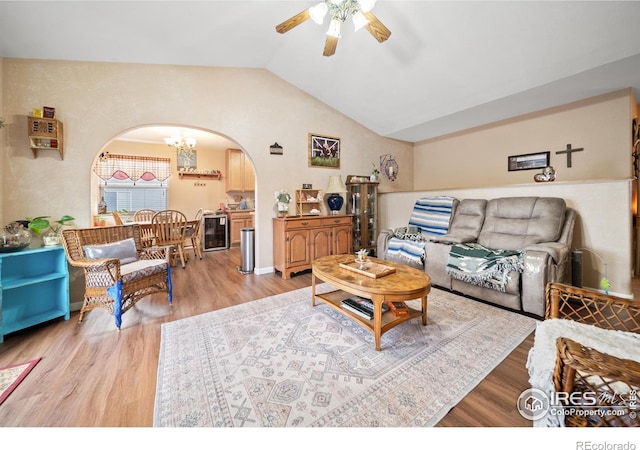 living room with ceiling fan with notable chandelier, light hardwood / wood-style flooring, beverage cooler, and vaulted ceiling