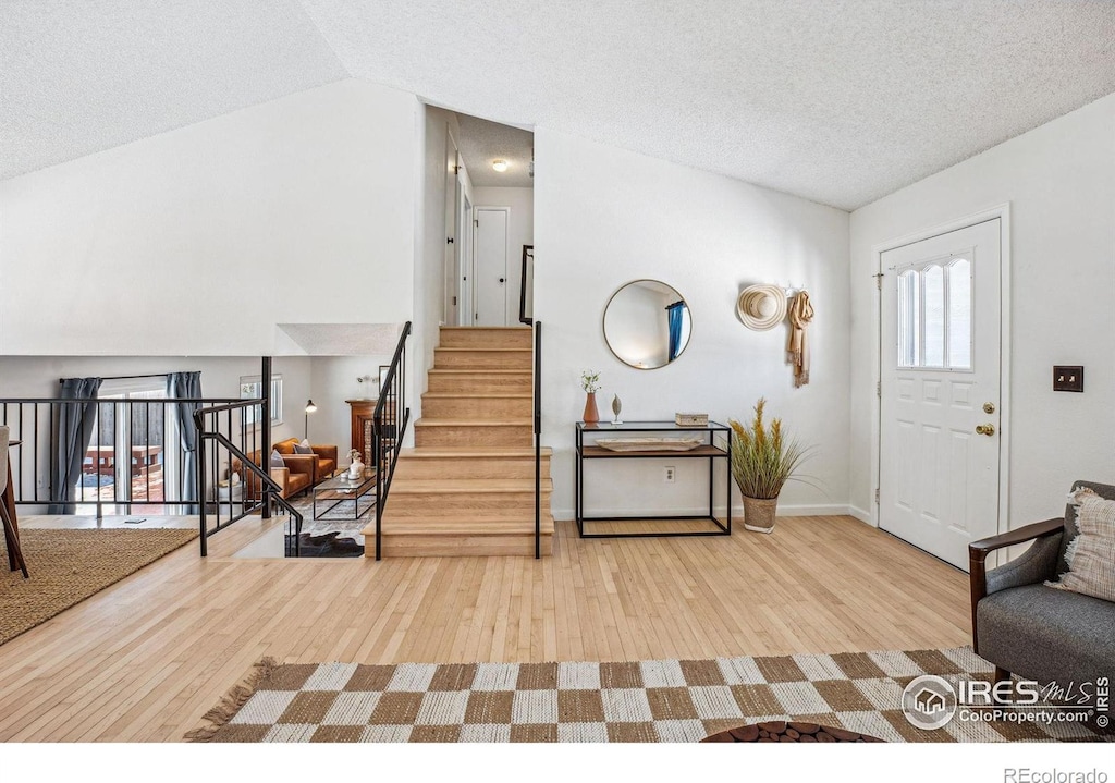 foyer entrance featuring hardwood / wood-style flooring, vaulted ceiling, and a textured ceiling