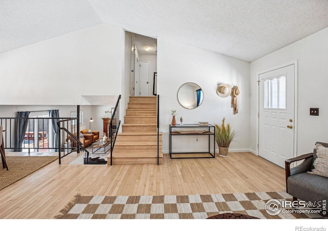 foyer entrance featuring hardwood / wood-style flooring, vaulted ceiling, and a textured ceiling