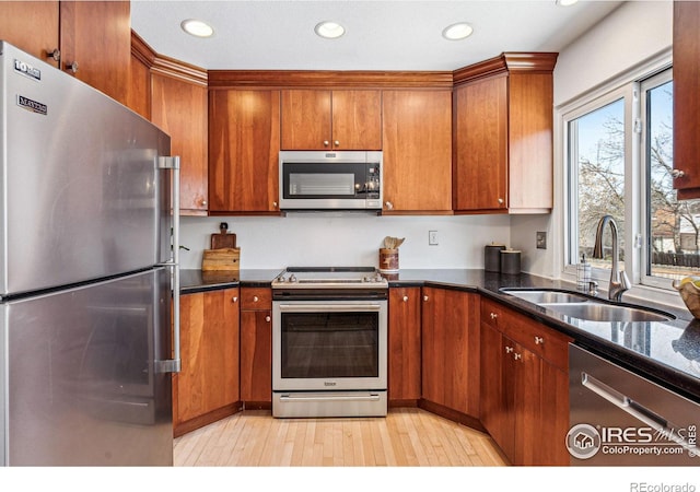 kitchen featuring dark stone countertops, appliances with stainless steel finishes, sink, and light wood-type flooring