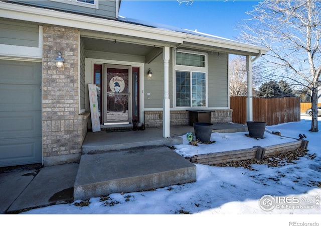 snow covered property entrance with a garage and covered porch