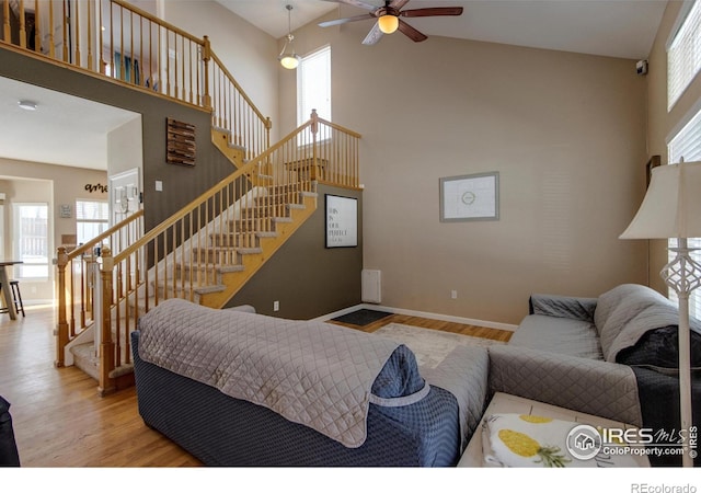 living room featuring ceiling fan, a towering ceiling, light hardwood / wood-style floors, and a wealth of natural light