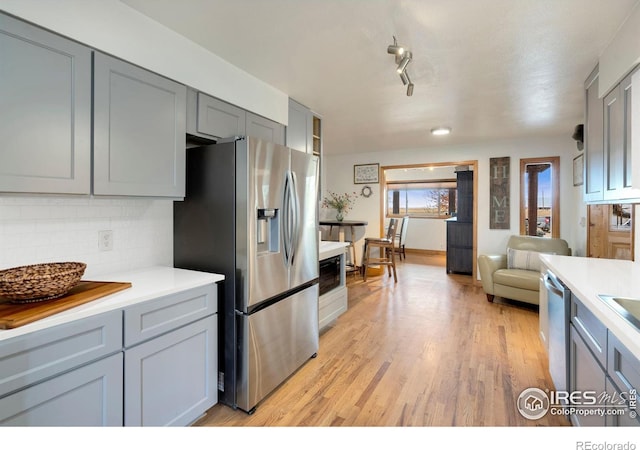 kitchen with gray cabinets, tasteful backsplash, appliances with stainless steel finishes, and light hardwood / wood-style floors