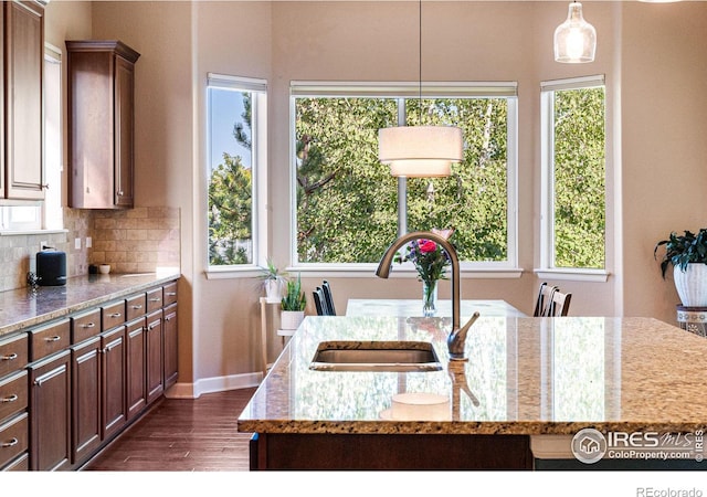 kitchen featuring light stone counters, sink, a kitchen island with sink, and pendant lighting