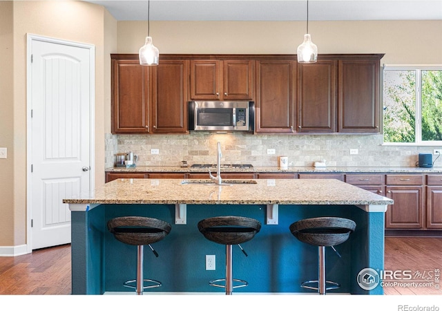 kitchen with light stone counters, decorative backsplash, a breakfast bar area, and a center island with sink