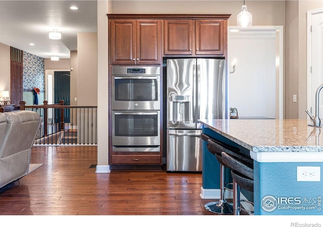 kitchen featuring dark wood-type flooring, appliances with stainless steel finishes, a kitchen bar, and light stone counters