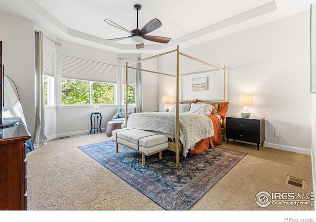 carpeted bedroom featuring ceiling fan and a tray ceiling