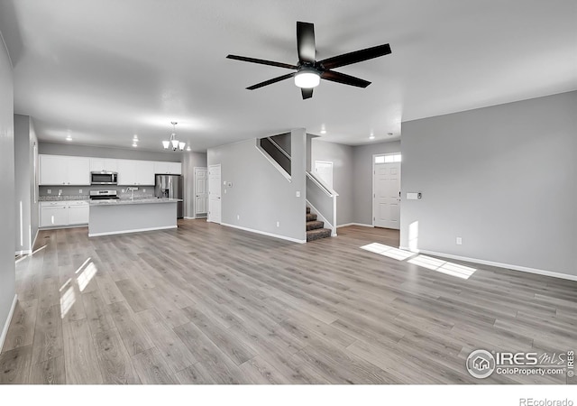 unfurnished living room featuring ceiling fan with notable chandelier and light hardwood / wood-style floors