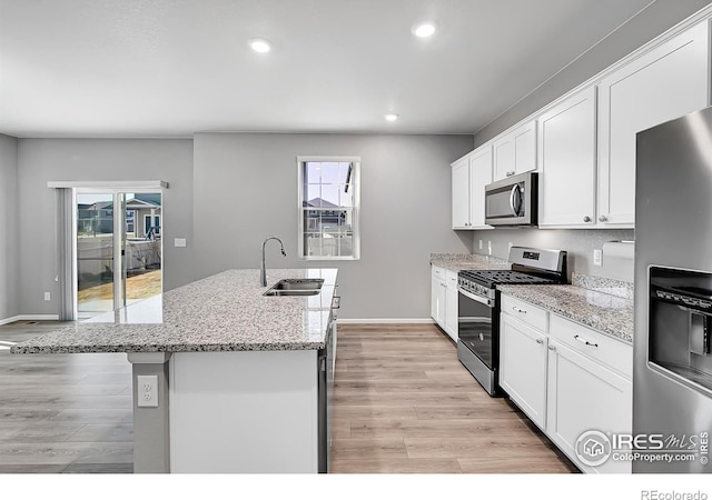 kitchen featuring an island with sink, white cabinetry, sink, light stone counters, and stainless steel appliances