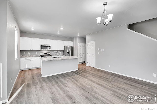 kitchen featuring sink, a kitchen island with sink, stainless steel appliances, white cabinets, and decorative light fixtures