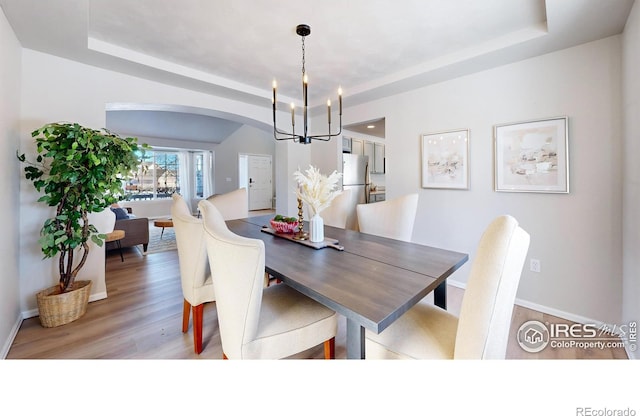 dining room featuring an inviting chandelier, light hardwood / wood-style flooring, and a raised ceiling