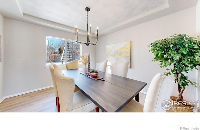 dining area with a notable chandelier, light hardwood / wood-style floors, and a tray ceiling