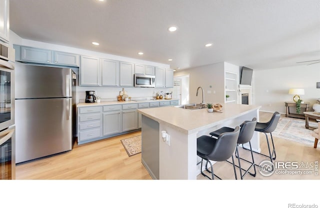 kitchen featuring a kitchen bar, sink, an island with sink, stainless steel appliances, and light hardwood / wood-style floors