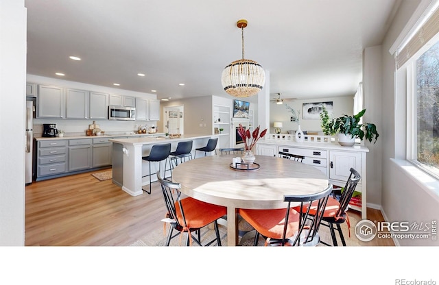 dining area with ceiling fan with notable chandelier and light wood-type flooring