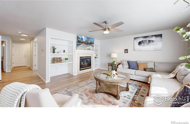 living room with built in features, ceiling fan, and light hardwood / wood-style flooring